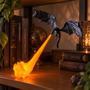 May include: A black dragon figurine in flight, suspended in the air, emitting a bright, glowing orange stream of fire that pools at the base. The dragon features textured wings and a long tail, with the light source creating a warm, vivid effect.