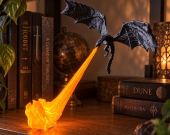 May include: A black dragon figurine in flight, suspended in the air, emitting a bright, glowing orange stream of fire that pools at the base. The dragon features textured wings and a long tail, with the light source creating a warm, vivid effect.