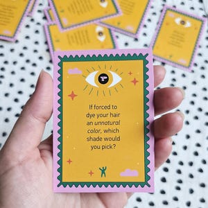 Pode incluir: Um cartão retangular com uma borda rosa recortada e um centro amarelo. O cartão apresenta um ícone de olho com um ponto de interrogação como pupila, pequenas estrelas e nuvens. O texto diz: If forced to dye your hair an unnatural color, which shade would you pick?