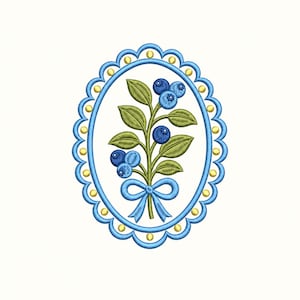 Puede incluir: Un diseño de bordado ovalado que presenta una rama central de arándanos con hojas verdes y bayas azules, atada con un lazo azul en la base. La rama está encerrada en un marco azul festoneado decorado con pequeños puntos amarillos.