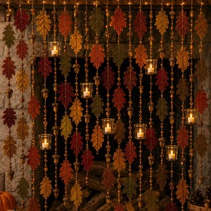 May include: A decorative hanging curtain featuring vertical strands of artificial autumn leaves in shades of red, orange, yellow, and green, interspersed with small brown acorn beads and clear glass votive candle holders with lit candles.
