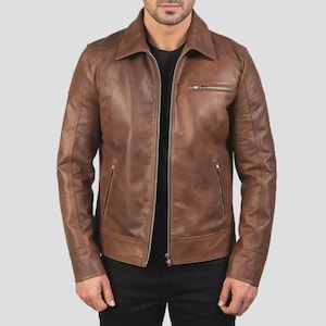 Könnte beinhalten: Eine braune Lederjacke mit klassischem Kragen, durchgehendem Frontreißverschluss und langen Ärmeln. Das Kleidungsstück verfügt über eine horizontale Reißverschlusstasche auf der linken Brustseite sowie zwei vertikale Reißverschlusstaschen.