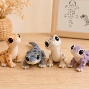 Peut inclure: Quatre petites figurines de geckos en feutre aiguilleté avec de grands yeux noirs et des motifs tachetés. Les geckos sont colorés dans des tons orange clair, gris, crème et violet. Chaque figurine a une surface texturée et une posture alerte.