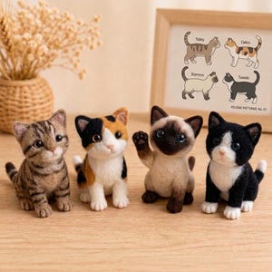 May include: Four needle-felted cat figurines in tabby, calico, Siamese, and tuxedo patterns. A framed print behind them displays these four cat types with the text Tabby, Calico, Siamese, Tuxedo, and FELIDAE PATTERNS: No. C1.