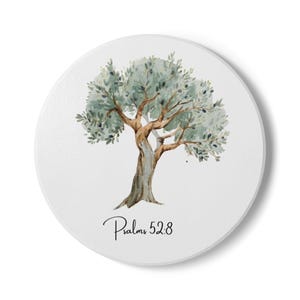 May include: A round white coaster featuring a watercolour illustration of an olive tree with green leaves and dark fruit. Below the tree, the text "Psalms 52:8" is printed in a black script font. The design is centred on the smooth surface.
