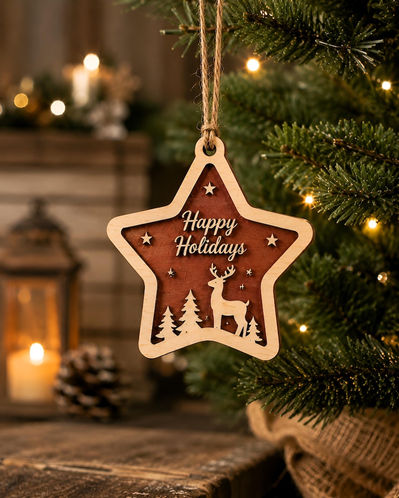 Op de afbeelding: Een stervormig houten ornament met een donkerbruin middenstuk waarin een hert en dennenbomen zijn uitgesneden. De tekst Happy Holidays is in het midden gegraveerd. Het ornament heeft een lichte houten rand en hangt aan een touwtje van jute.