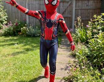 Può includere: Un costume completo di Spider-Man composto da una tuta rossa e blu con un emblema di ragno nero sul petto, dettagli color oro e una maschera rossa abbinata con grandi lenti oculari bianche, indossato in una posa con un braccio teso.