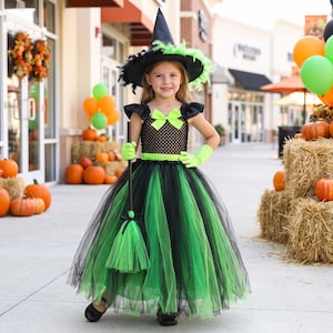 May include: A black and neon green witch costume featuring a floor-length tulle skirt, a bodice with a black mesh overlay, a bright green bow at the neckline, matching neon green gloves, a pointed witch hat with green feathers, and a broom prop.