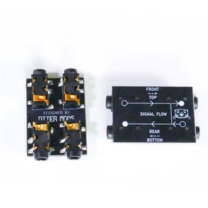 Pu&ograve; includere: Due schede jack audio nere con connettori dorati e la scritta "DESIGNED BY OTTER MODS". Una scheda ha quattro jack, l'altra ha due jack e la scritta "SIGNAL FLOW" con una grafica di lontra.