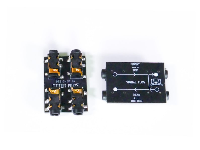 Pu&ograve; includere: Due schede jack audio nere con connettori dorati e la scritta "DESIGNED BY OTTER MODS". Una scheda ha quattro jack, l'altra ha due jack e la scritta "SIGNAL FLOW" con una grafica di lontra.