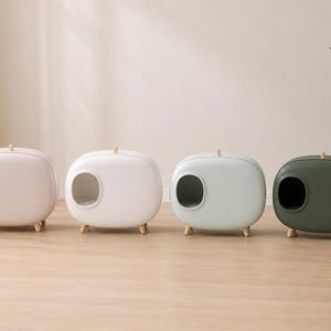 Puede incluir: Cuatro casas para mascotas de forma ovalada con bordes redondeados, cada una con una entrada lateral circular, un pequeño asa en la parte superior y cuatro patas cortas de madera. Las unidades se presentan en colores rosa pastel, blanco, azul claro y verde bosque.