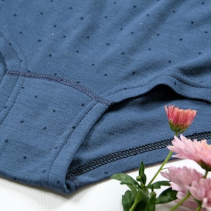 May include: Close-up of a blue cotton underwear with a small white polka dot pattern. The underwear has a dark blue elastic waistband and a dark blue seam around the leg openings.