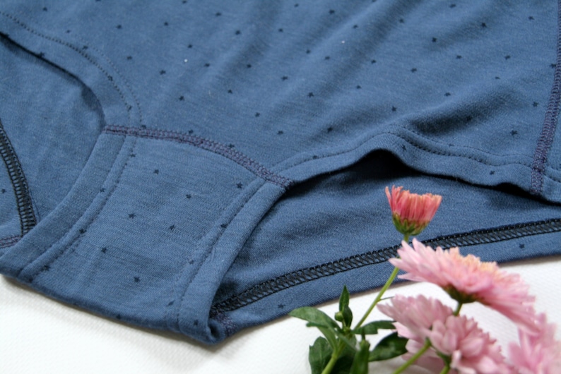 May include: Close-up of a blue cotton underwear with a small white polka dot pattern. The underwear has a dark blue elastic waistband and a dark blue seam around the leg openings.
