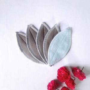 May include: Five reusable makeup remover pads in a leaf shape. Four are gray with white stitching and one is light blue with white stitching.