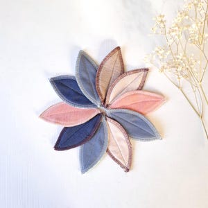 May include: A set of six reusable cloth menstrual pads in a variety of colors, including pink, blue, and brown. The pads are shaped like leaves and are arranged in a circle.