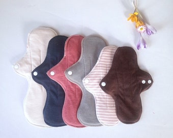 May include: Six reusable cloth menstrual pads in various colors and patterns, including beige, black, red, gray, pink and brown. The pads are arranged in a row, with the beige pad at the top and the brown pad at the bottom.