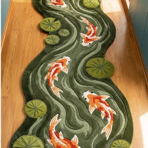 Pode incluir: Um tapete passadeira longo e sinuoso com um fundo verde profundo e padrões de água em espiral. O tapete é decorado com vários peixes koi laranja, brancos e pretos a nadar em diferentes direções, intercalados com nenúfares verdes redondos.