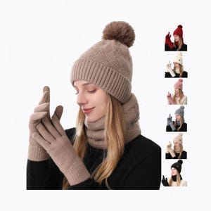 May include: A beige knit beanie with a matching pom-pom, a ribbed cuff, and a textured basketweave pattern, paired with a matching ribbed neck warmer and knit gloves. The set is shown in multiple color variations including red, white, pink, and gray.