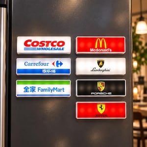 Può includere: Un set di sette magneti rettangolari con vari loghi di marchi, tra cui Costco, McDonald's, Carrefour, FamilyMart, Lamborghini, Porsche e Ferrari. Ogni magnete ha una combinazione di colori distinta ed è disposto su una superficie scura.