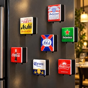 May include: A collection of seven square, illuminated refrigerator magnets featuring various beverage brand logos including Asahi, Budweiser, Kronenbourg 1664, Heineken, Coca-Cola, and Corona Extra. Each magnet has a black frame and a white light-up face.