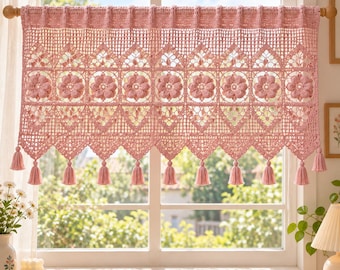 May include: A dusty rose crochet valance curtain featuring a repeating pattern of floral motifs, intricate openwork lattice, and a scalloped bottom edge finished with small hanging tassels. The curtain is suspended from a wooden rod.