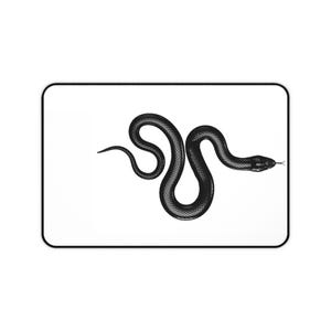 Può includere: Un tappetino da scrivania rettangolare con sfondo bianco, bordo nero e un'illustrazione nera dettagliata di un serpente al centro. Il serpente è raffigurato in una posa sinuosa a forma di S, con la testa rivolta verso il lato destro.