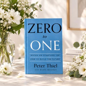 May include: A hardcover book titled Zero to One: Notes on Startups, or How to Build the Future by Peter Thiel with Blake Masters. The book cover is bright blue with bold black and white text, standing upright in a clear glass vase with white flowers.