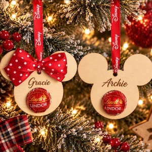 May include: Two light-coloured wooden ornaments shaped like mouse heads, each featuring a red Lindt Lindor chocolate ball in the centre. One ornament has a red and white polka dot bow and the name Gracie, while the other has the name Archie.