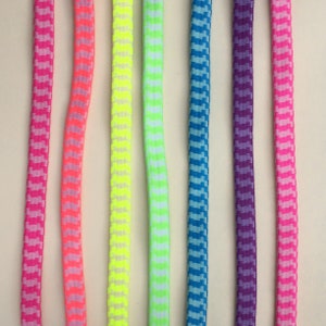 Pode incluir: Sete cadarços de diferentes cores, incluindo rosa, rosa claro, amarelo, verde, azul, roxo e rosa choque. Cada cadarço tem um padrão xadrez branco.