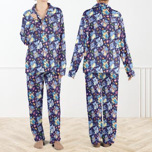 May include: A two-piece pajama set featuring a long-sleeved button-down shirt with a collar and matching long pants. The fabric is dark blue and decorated with a repeating pattern of light blue cartoon creatures, pink coral, and yellow stars.