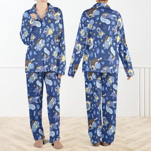 May include: A two-piece pajama set featuring a long-sleeved button-down shirt and matching pants in a dark blue color. The fabric is covered in a repeating pattern of light blue turtle-like creatures, yellow stars, and small aquatic icons.