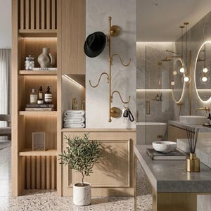 Puede incluir: Un perchero de pared vertical de latón con tres ganchos curvos, que sostiene un sombrero fedora negro y un juego de llaves. El perchero está montado en una pared de color claro junto a estanterías de madera con objetos decorativos y toallas blancas.