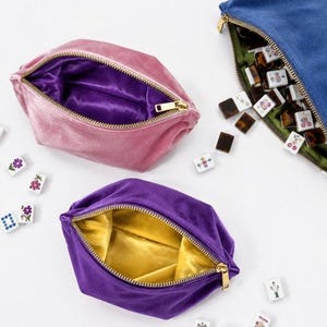 Può includere: Tre pochette con cerniera in velluto rosa, viola e blu, ciascuna con una fodera in raso a contrasto. La pochette rosa ha un interno viola, quella viola un interno giallo e quella blu un interno verde, accompagnate da tessere del mahjong.