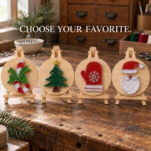 May include: Four circular wooden plaques on small easels, each featuring a holiday string art design: a candy cane, a Christmas tree, a red mitten with a snowflake, and a Santa face. The text CHOOSE YOUR FAVORITE is displayed above the items.