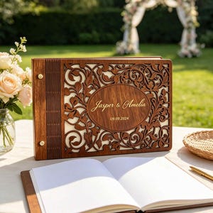 May include: A rectangular wooden photo album with a laser-cut floral pattern and a central oval plaque engraved with the text Jasper & Amelia and the date 09.09.2024. The album features a dark brown wood finish, gold-toned metal binding screws.