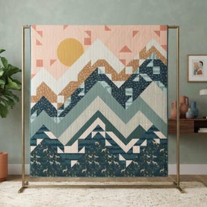 May include: A rectangular quilt featuring a geometric mountain landscape design. The pattern displays layered peaks in shades of dark blue, sage green, tan, and white, with a large yellow sun against a pale pink sky filled with scattered triangles.
