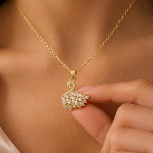 May include: A gold-toned necklace featuring a swan-shaped pendant. The swan is embellished with numerous small, clear, marquise-cut stones along its body and wing, with tiny round stones accenting the neck and head, suspended from a delicate chain.