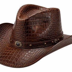 Pode incluir: Um chapéu de cowboy castanho escuro com um padrão texturizado de pele de crocodilo na copa e na aba. O chapéu inclui uma faixa castanha a condizer, decorada com pequenos tachas metálicas e um ornamento circular central com uma pedra preta.