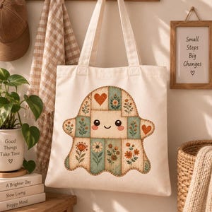 A canvas tote bag hangs on a wooden peg rack, displaying a printed graphic of a vintage floral patchwork ghost with a smiling face.