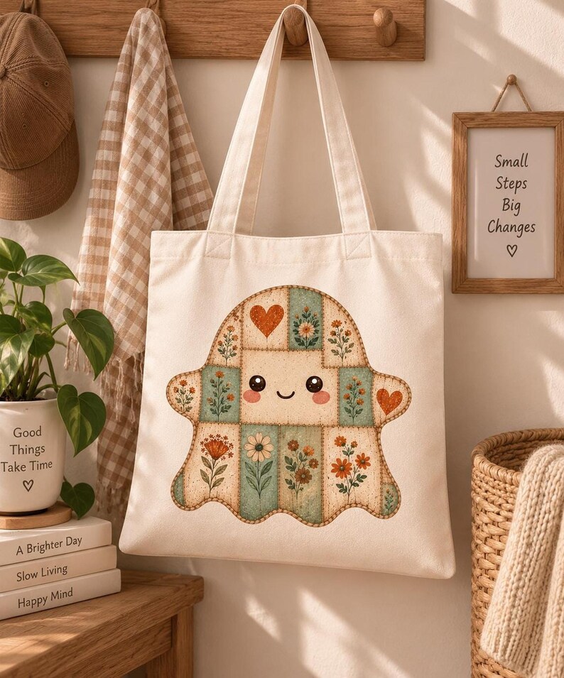 A canvas tote bag hangs on a wooden peg rack, displaying a printed graphic of a vintage floral patchwork ghost with a smiling face.