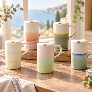 May include: Five ceramic mugs with lids, each featuring a two-tone gradient design. The colours include white paired with soft pink, yellow, green, blue, and a speckled olive green. Each mug has a side handle and a flat lid with a small opening.