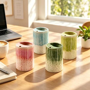 May include: Four cylindrical ceramic pen holders with a vertical ribbed texture and a two-tone glaze. Each holder features a smooth, coloured top section that fades into a speckled white base, with a small circular hole near the rim.