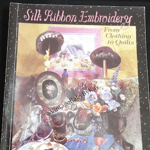 May include: A softcover book titled Silk Ribbon Embroidery From Clothing to Quilts by Piecemakers. The cover features a collage of embroidered items including hats, a framed floral piece, a denim shirt, and various fabric accessories with floral designs.