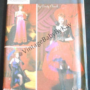 May include: A Simplicity Costumes sewing pattern envelope by Cindy Chock featuring three distinct costume designs. The cover displays photographs of outfits including a pink gown, a purple corset dress, and a red skirt ensemble with black accents.