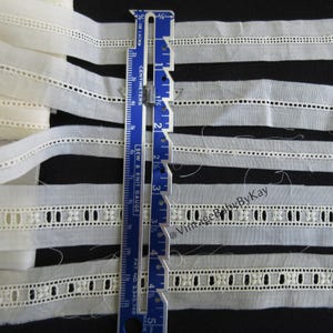 May include: Five white cotton lace trims with a scalloped edge. The trims are arranged in a stack and measured with a ruler. The trims are approximately 1/2 inch wide.