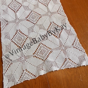 May include: Cream-colored, open-weave crochet table runner with a geometric diamond pattern. The runner is rectangular with a scalloped edge. The text "VintageBabyByKay" is printed on the runner.