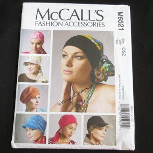 May include: McCall's Fashion Accessories pattern M6521. The pattern features various headwear designs, including caps and head wraps. The image showcases different styles, such as a pink head wrap, a blue cap, and a black cap with a white brim.
