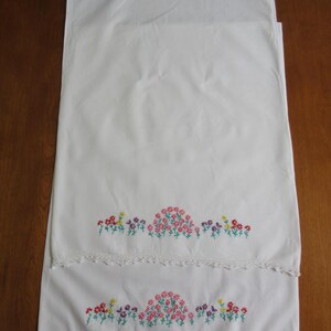 Pu&ograve; includere: Una coppia di federe rettangolari bianche con un motivo floreale ricamato a mano lungo il bordo inferiore. Il ricamo mostra piccoli fiori rossi, rosa, viola e gialli con steli verdi. Ogni federa presenta un bordo in pizzo bianco lavorato all'uncinetto.