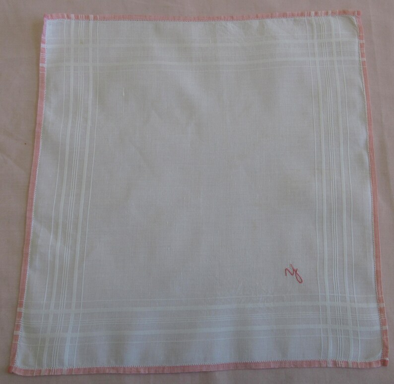 May include: White cotton handkerchief with a pink border and a pink embroidered initial "R" in the lower right corner.