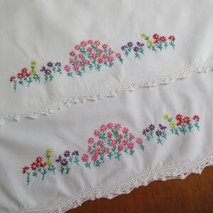 Pu&ograve; includere: Due pannelli di tessuto bianco con delicati ricami floreali nei toni del rosa, rosso, giallo e viola con steli verdi. Ogni pannello &egrave; rifinito con un bordo decorativo in pizzo all'uncinetto bianco lungo il margine inferiore del tessuto.